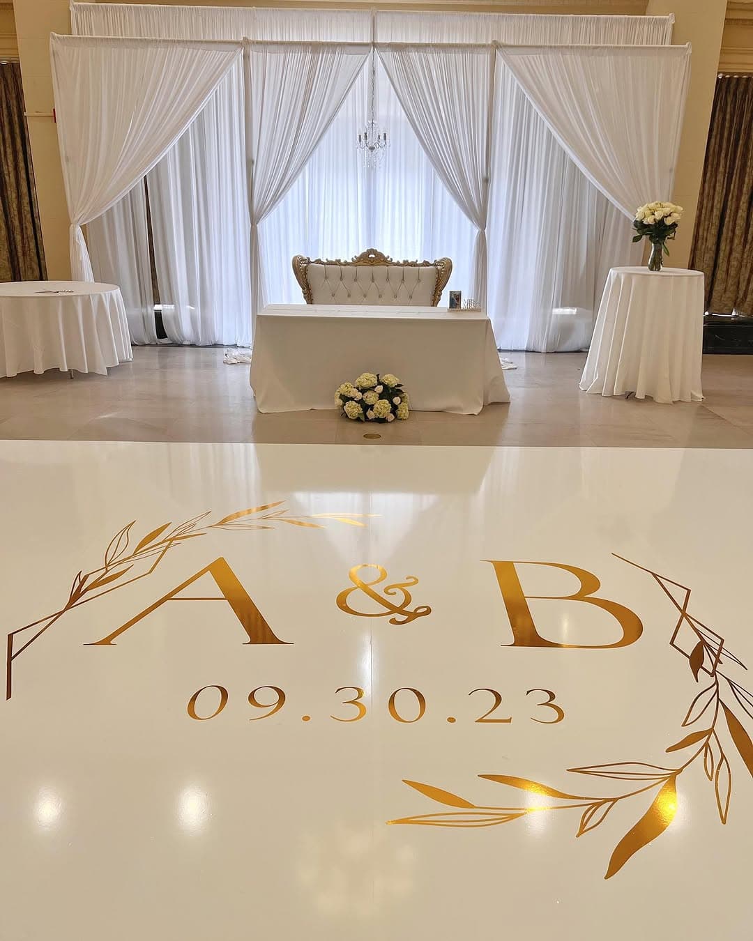 Cream dance floor rental printed with a gold monogram, wedding date and olive-branch wreath at a reception