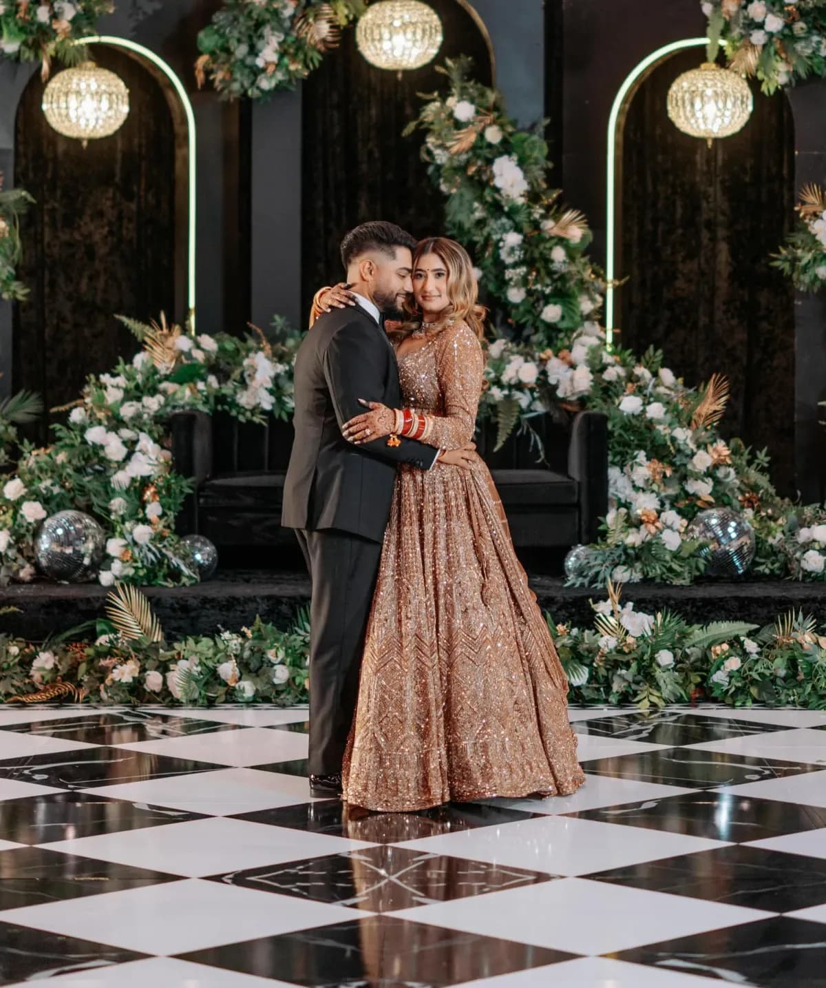 Couple dancing on elegant black and white checkered dance floor wrap with crystal chandeliers and lush floral backdrop