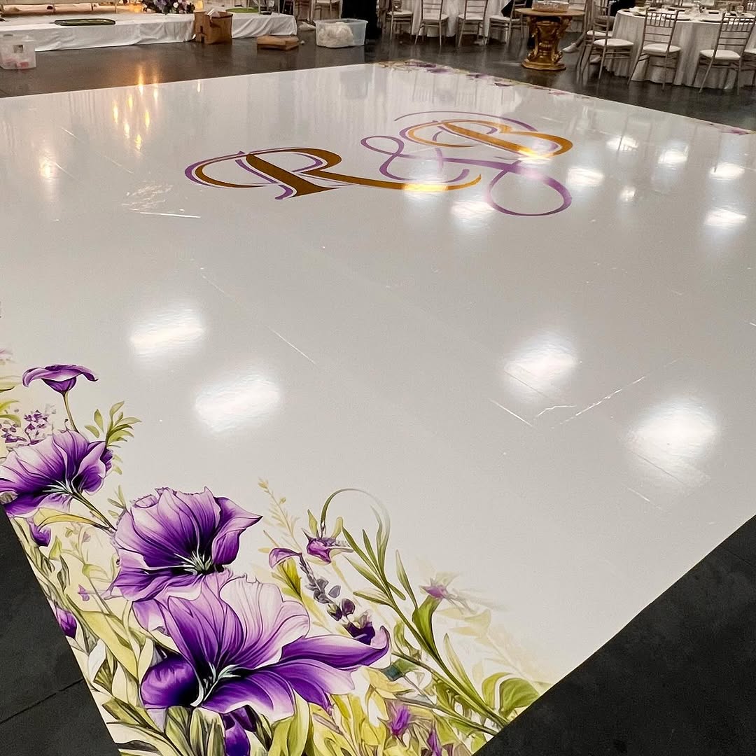 Luxury custom dance floor rental in glossy white with a gold monogram and painted lily border, installed for a Fresno event